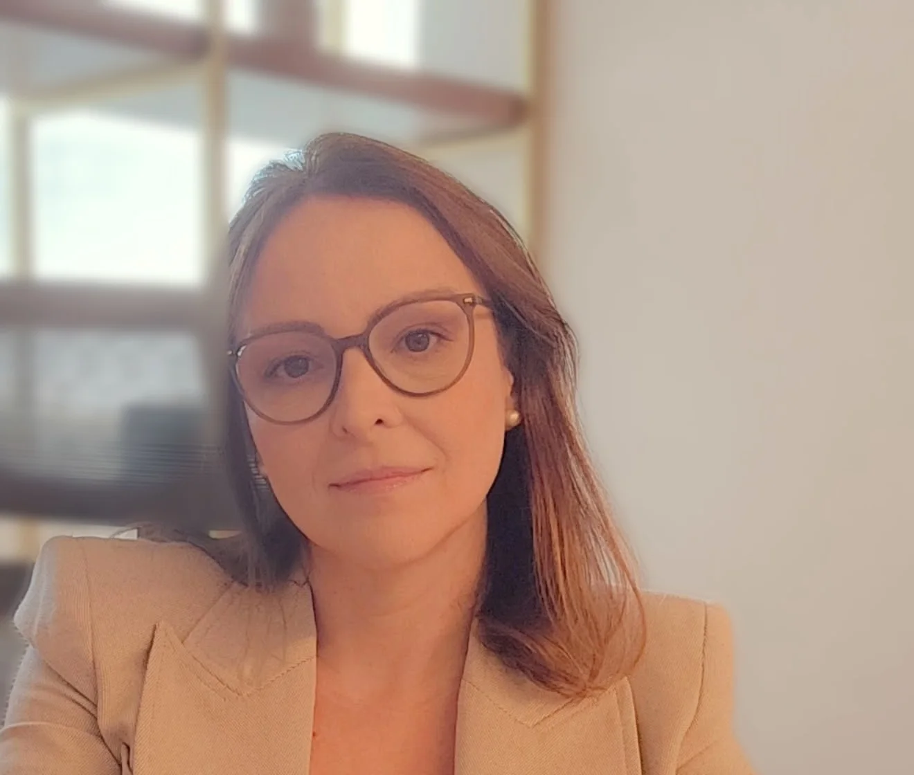 Dra. Ana Emília Pinheiro, de óculos e blazer bege, à mesa do consultório
